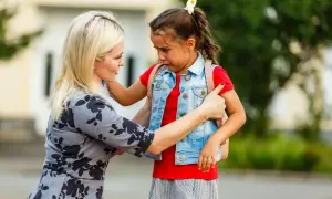 Mutter tröstet weinendes Kind mit Trennungsangst vor der Schule.
