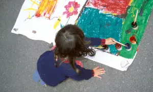 Ein Kind malt auf einem großen Blatt Papier. Die bunten Farben und die Art der Zeichnung könnten auf die Verarbeitung von kinderzeichnungen trauma hindeuten.
