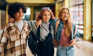 Drei lachende Freunde gehen Arm in Arm durch einen Flur. Sie sind im perfekten Alter, um zu sagen: ab wann ist man jugendlich?