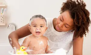 Mutter wäscht ihr Baby mit Schaum und Quietscheente. Ein warmes Bad kann bei Fieber helfen.