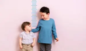 Zwei Jungen stehen vor einer Messlatte. Der ältere Junge, vielleicht 4 Jahre alt, legt dem kleineren seine Hand auf die Schulter.