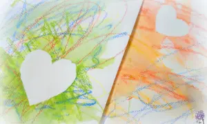 Bunte Kritzeleien, wie Kinder sie malen, mit weißen Herzen darauf. Ein Herz auf grünem, das andere auf orangem Hintergrund.