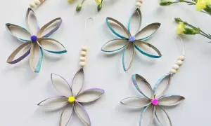 Bunte Blumen aus Klopapierrollen basteln: Vier hübsche Anhänger mit Holzperlen und Pompons, umgeben von gelben Blüten.