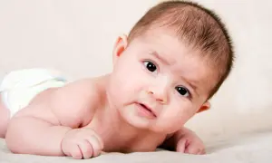 Ein süßes Baby, 4 Wochen alt, liegt auf dem Bauch und blickt neugierig in die Kamera.
