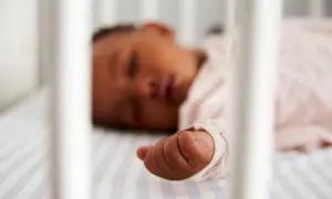 Ein Baby zuckt im Schlaf, seine kleine Hand liegt auf gestreifter Bettwäsche.