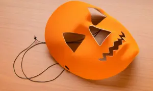 Orange halloween maske basteln: Kürbisgesicht mit Zackenmund und dreieckigen Augen auf Holzhintergrund.