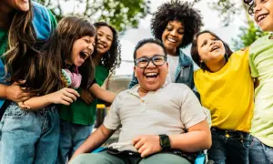 Fröhliche Kinder lachen und umarmen sich. Ein Junge im Rollstuhl strahlt. Wann ist Weltkindertag? An diesem Tag feiern wir alle Kinder!