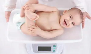 Ein lächelndes Baby liegt auf einer Waage für die U3 Untersuchung. Hände halten das Kind sanft.
