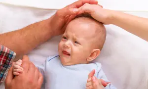 Ein weinendes Baby, 7 Wochen alt, wird von Elternhänden gehalten und getröstet.