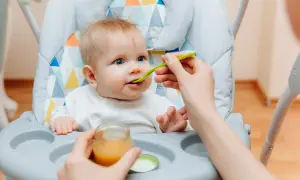 Ein süßes Baby von 6 Monaten sitzt im Hochstuhl und bekommt Brei gefüttert.