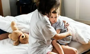 Mutter tröstet ihr Kind, das eine panikattacke hat. Ein Teddybär liegt daneben.