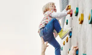 Kleines Kind klettert an einer Boulderwand, fördert seine Kompetenz. Hände helfen und sichern.