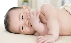 Ein süßer **baby 11 wochen** alt liegt auf der Seite und bedeckt seinen Mund mit der Hand.