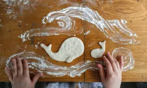 Kinderhände gestalten Salzteig-Ideen: zwei Wale schwimmen in Meereswellen aus Mehl auf einem Holztisch.