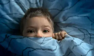 Ein Kind versteckt sich ängstlich unter der Decke. Ab wann haben Kinder Angst im Dunkeln?
