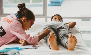 Kinder spielen Doktorspiele im Kindergarten. Ein Mädchen in Arztkittel untersucht einen Jungen, der auf einer Liege liegt.