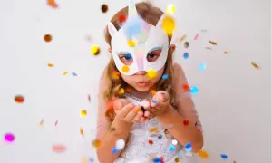 Kind mit Einhorn-Maske pustet Konfetti. Perfekt für Ideen zum Masken basteln, Vorlagen ausdrucken und eine magische Feier.
