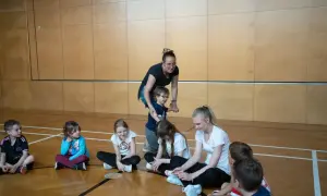 Lehrerin fördert die psychomotorik kinder in der Turnhalle. Kinder sitzen auf dem Boden und hören aufmerksam zu.