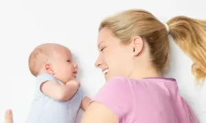 Ein lächelnder baby 2 wochen alt schaut seine Mutter an. Sie liegt neben ihm und lächelt zurück.
