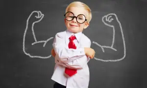 Kleiner Junge mit Brille und Krawatte, selbstbewusst vor Kreidezeichnungen starker Arme. So bekommt mein Kind mehr Selbstbewusstsein.