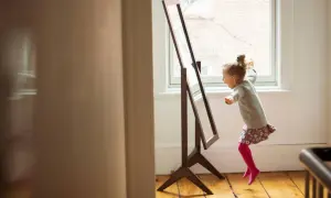 Ein kleines Mädchen springt vor einem Spiegel und lacht. Dieses Bild zeigt, wie sehr das Spielen mit dem Spiegelbild das Kind glücklich macht.
