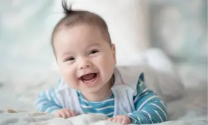Ein fröhliches Baby, 21 Wochen alt, liegt auf dem Bauch und lacht herzhaft.