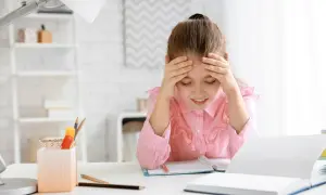 Ein Mädchen mit Händen an der Stirn, das über seinen Büchern sitzt. Die **Stress Kinder** sind deutlich zu sehen.