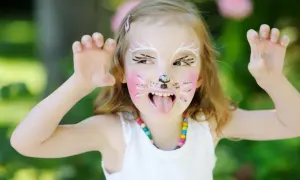 Ein Kind mit süßem Katzen-Make-up, das mit den Pfoten nach oben zeigt. Das Kind hat rosa Wangen, Schnurrhaare und eine schwarze Nase.