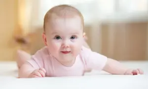 Ein süßes Baby mit blauen Augen liegt auf dem Bauch und versucht, den Kopf zu halten. Es trägt ein rosa Body.