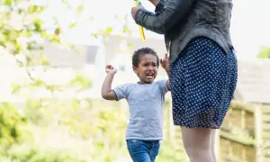 Ein 3-jähriger Junge schreit und hält die Arme hoch, während eine Frau Seifenblasen macht. Ein Moment der Entwicklung.