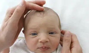 Sanft berühren die Hände eines Elternteils das Köpfchen eines Babys. Die Fontanelle ist leicht eingefallen, ein Zeichen für mögliche Dehydrierung.