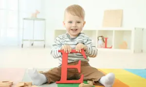 Ein lächelnder Junge hält den roten Buchstaben "E". Vielleicht ein zukünftiger Elias oder Emil, einer der vielen Jungennamen mit E.