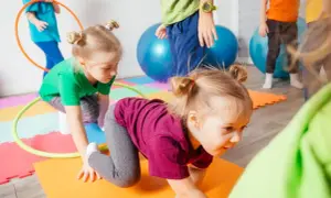 Kinder haben Spaß bei Bewegungsspielen im Kindergarten. Sie krabbeln auf bunten Matten, umgeben von Gymnastikbällen und Reifen.