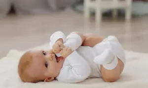 Ein süßes Baby, 8 Wochen alt, liegt auf einer weichen Decke und spielt mit seinen Füßen.