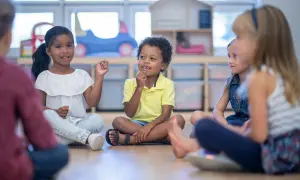 Kinder sitzen im Kreis und lernen. Die Lehrerin beobachtet aufmerksam, um die **Schulreife erkennen** zu können.