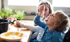 Große Schwester versucht, den kleinen Bruder zum Essen zu überreden, der nicht essen will.