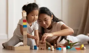 Mutter und Kind bauen mit Holzklötzen und Dinosauriern. Feinmotorik Kinder wird spielerisch gefördert.