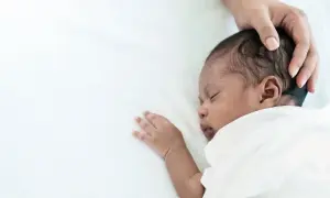 Ein süßes Baby schwitzt beim Schlafen am Kopf. Eine Hand streichelt sanft über das dunkle Haar.