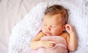 Ein schlafendes Baby, 9 Wochen alt, eingewickelt in eine rosafarbene Decke, liegt auf einer weißen, flauschigen Unterlage.
