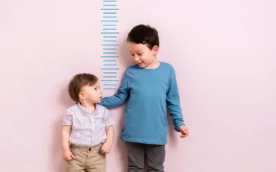Zwei Jungen stehen vor einer Messlatte. Der ältere Junge, vielleicht 4 Jahre alt, legt dem kleineren seine Hand auf die Schulter.