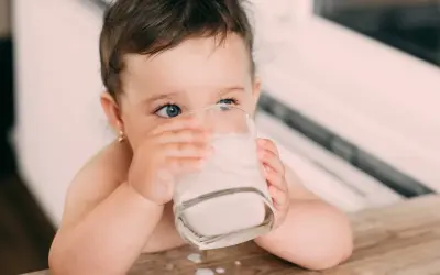 Kleines Kind trinkt aus einem Glas Milch. Die blauen Augen blicken neugierig. Baby Kuhmilch ist wichtig für das Wachstum.