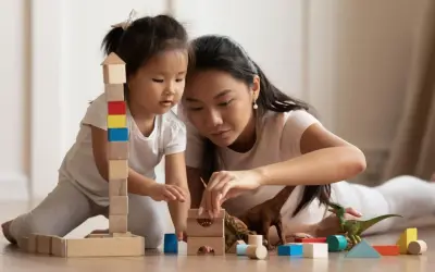 Mutter und Kind bauen mit Holzklötzen und Dinosauriern. Feinmotorik Kinder wird spielerisch gefördert.