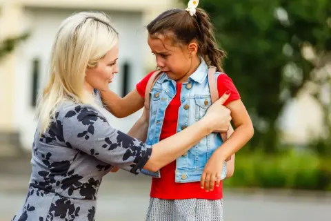 Mutter tröstet weinendes Kind mit Trennungsangst vor der Schule.