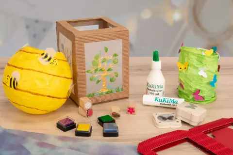 Bastelmaterialien für eine Laterne: Bienen-Laterne, Baum-Laterne, Kleber, Stempel & Schmetterlingsstanzer. Eine Vorlage zum Laterne basteln.