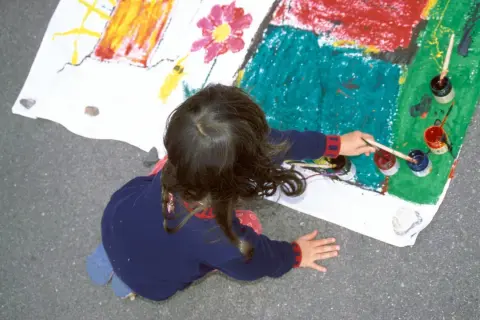 Ein Kind malt auf einem großen Blatt Papier. Die bunten Farben und die Art der Zeichnung könnten auf die Verarbeitung von kinderzeichnungen trauma hindeuten.
