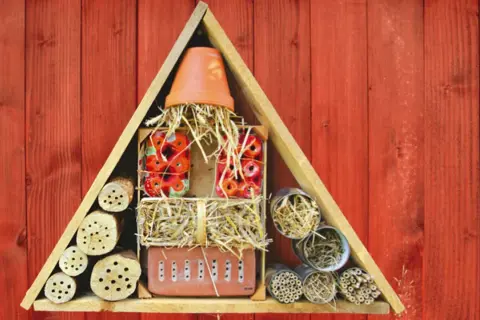 Ein selbstgebautes Insektenhotel für Kinder, gefüllt mit Holzstämmen, Stroh und Ziegeln, bietet Unterschlupf für nützliche Insekten.