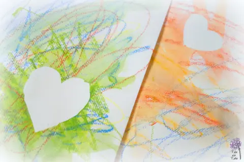 Bunte Kritzeleien, wie Kinder sie malen, mit weißen Herzen darauf. Ein Herz auf grünem, das andere auf orangem Hintergrund.