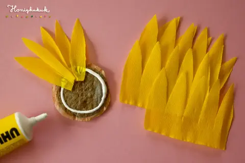 Sonnenblume basteln Krippe: Gelbe Blütenblätter aus Krepppapier werden auf einen Teebeutel geklebt.