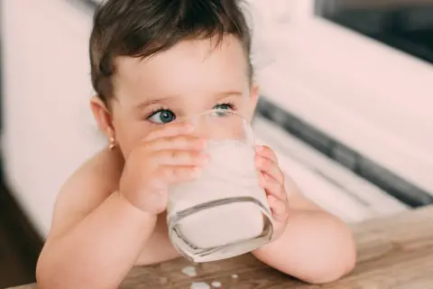 Kleines Kind trinkt aus einem Glas Milch. Die blauen Augen blicken neugierig. Baby Kuhmilch ist wichtig für das Wachstum.