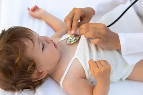 Arzt hört mit Stethoskop auf das Herz eines Babys. Eine U6 Untersuchung ist wichtig für die Gesundheit des Kindes.